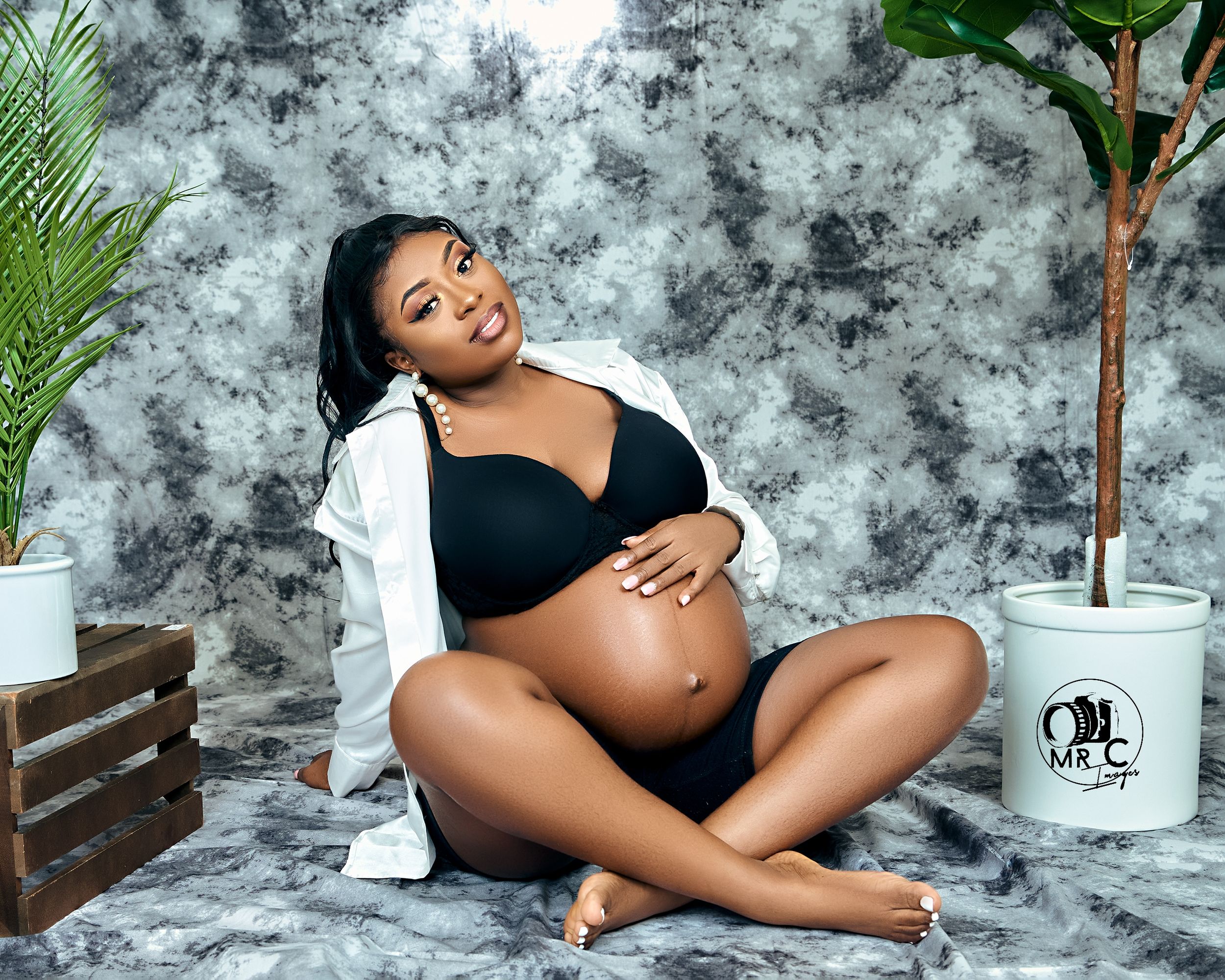 Intimate maternity photo with simple black attire against grey background with tropical plants.