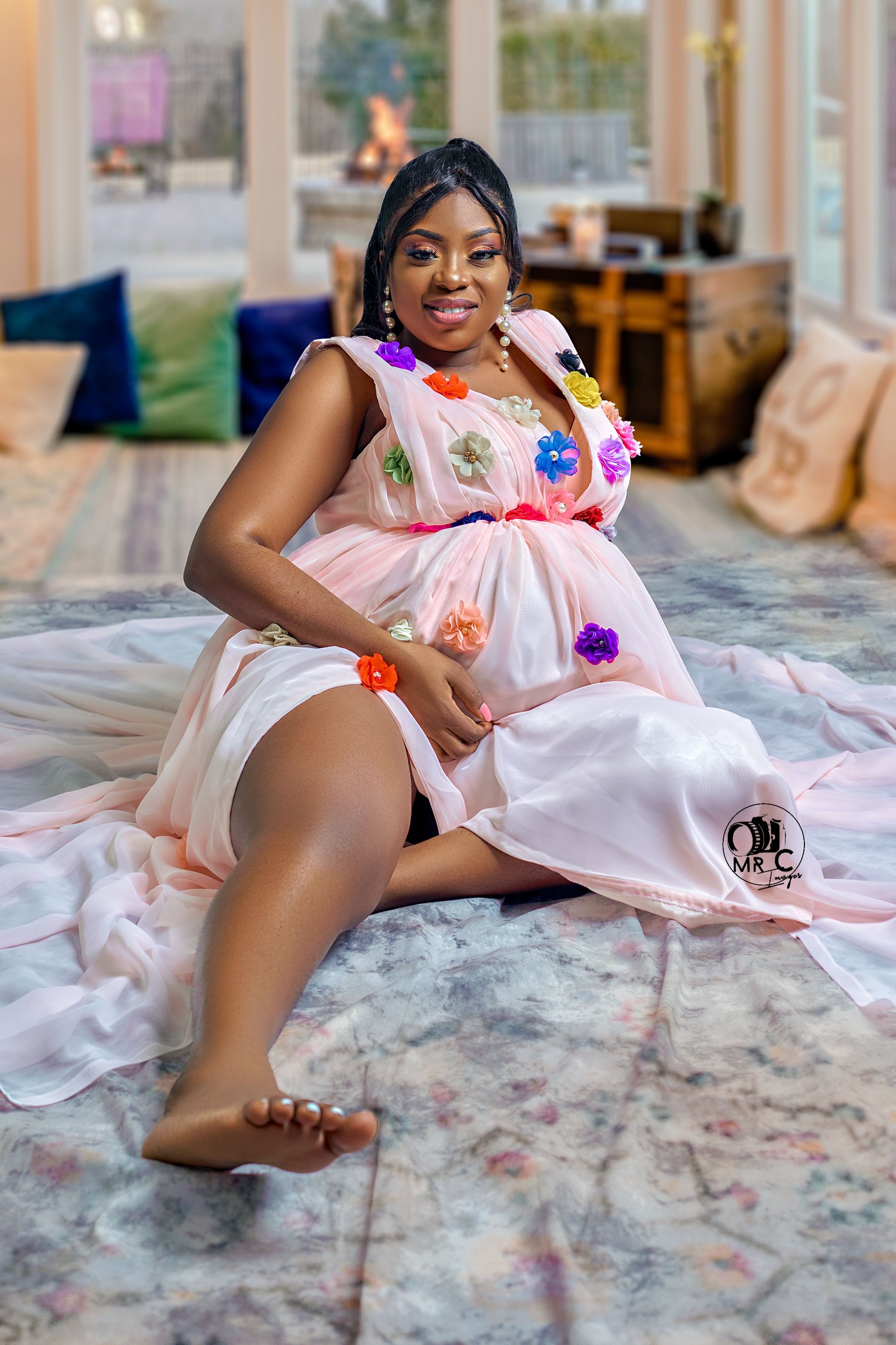 Maternity portrait in pink floral dress with colorful appliques on plush carpet.