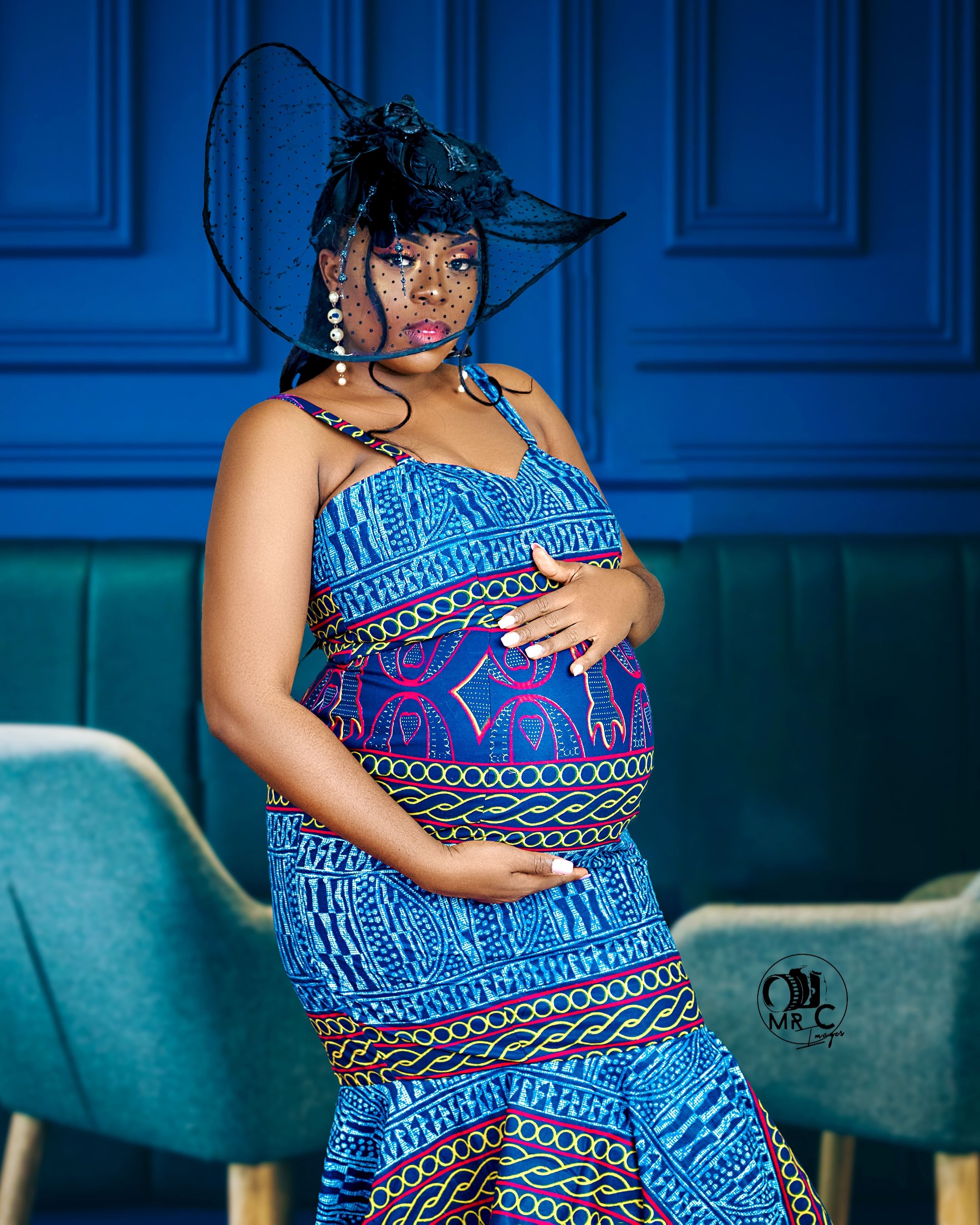 Maternity photo in blue patterned dress with tribal print against vibrant blue wall.