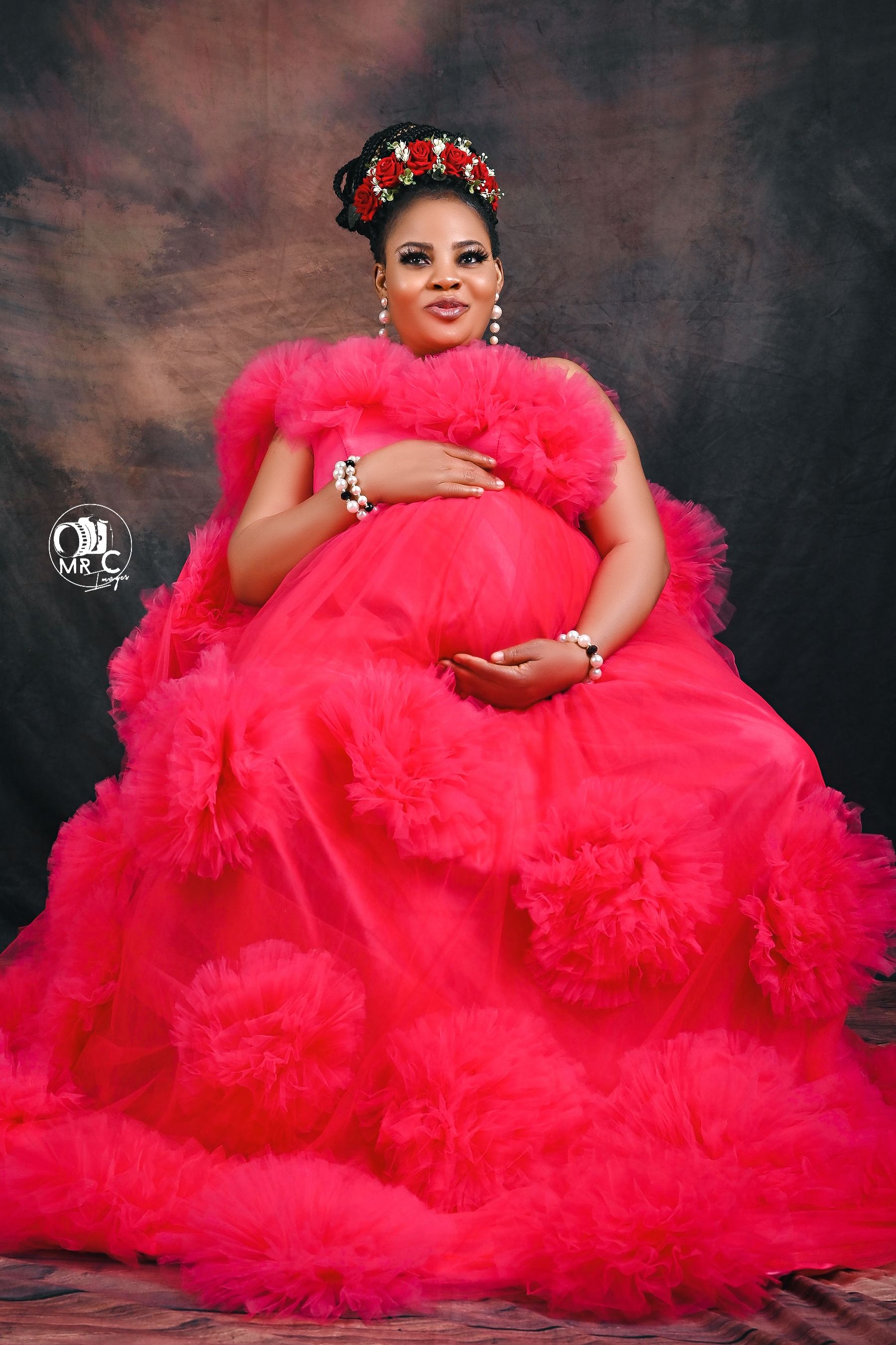 Glamorous red tulle ball gown maternity portrait with floral crown against dark backdrop.