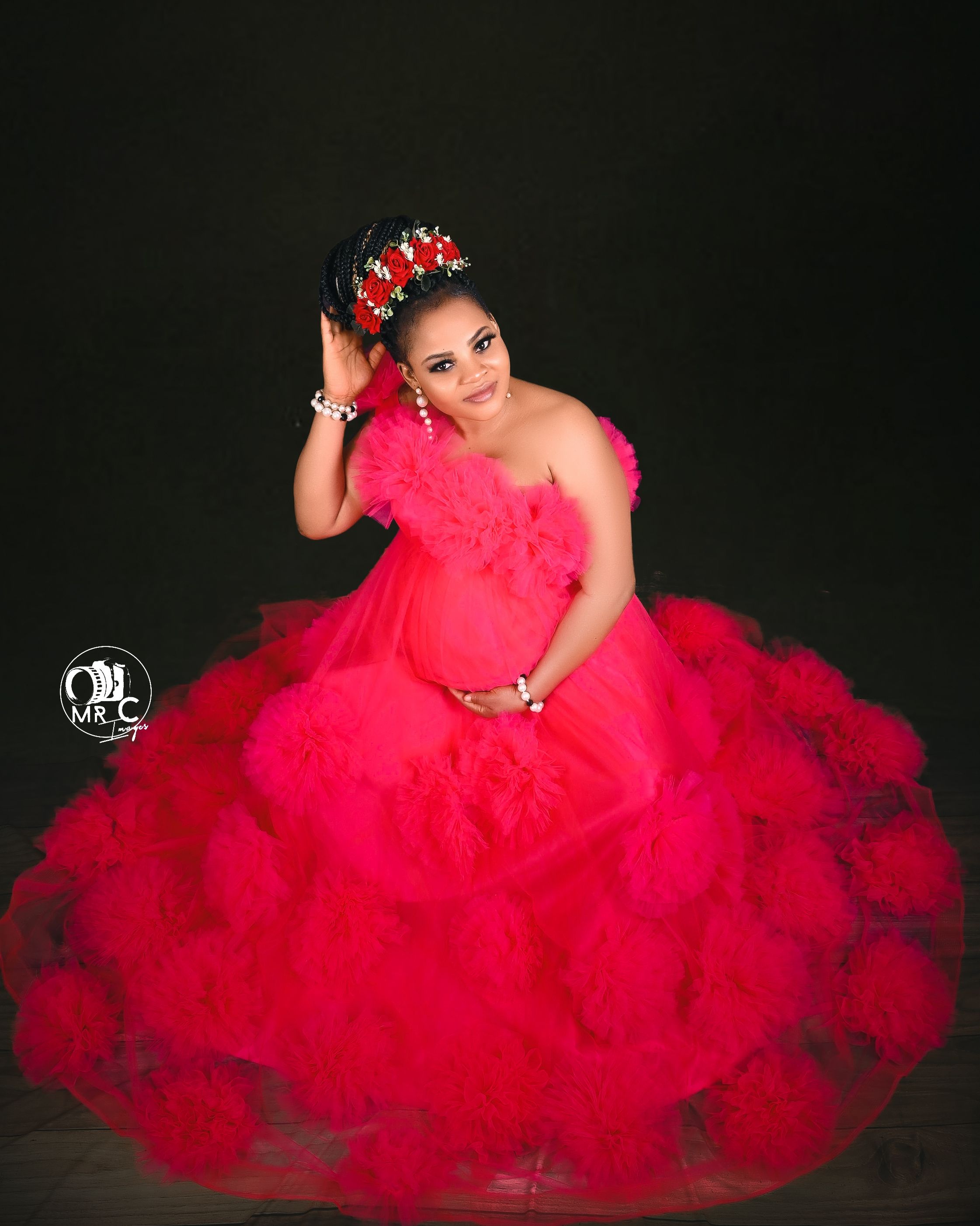 Studio portrait featuring dramatic red tulle maternity ball gown against black background.