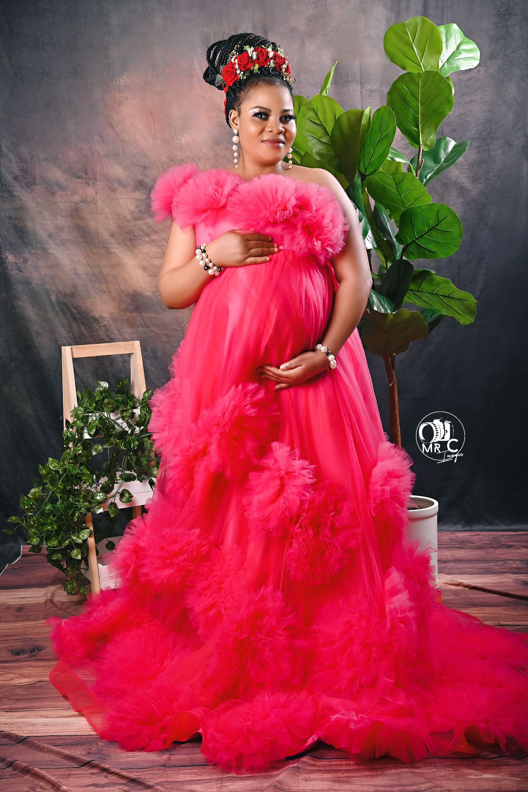 Dramatic red tulle maternity gown with floral headpiece in studio setting with green plant decor.