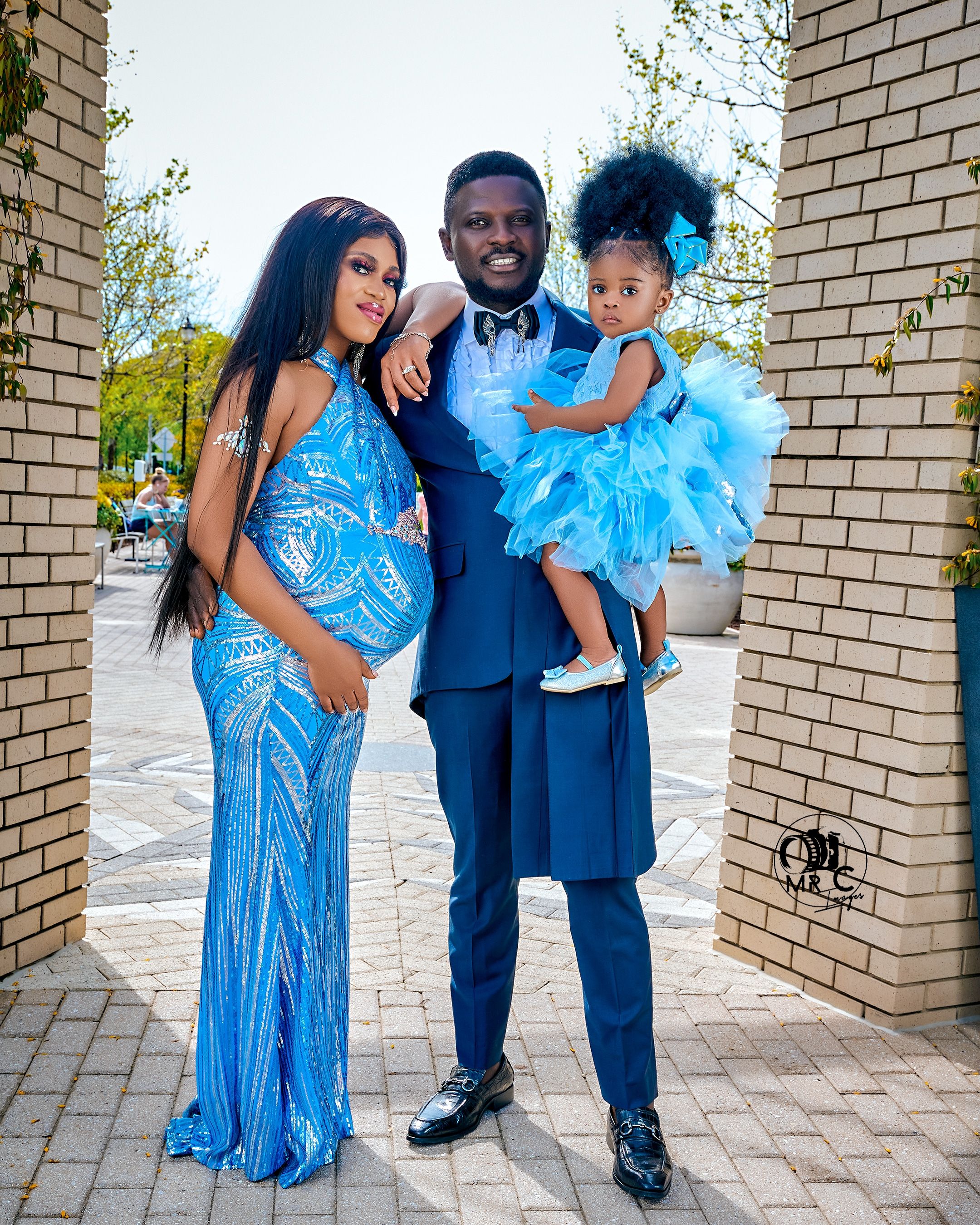 Family portrait featuring coordinating blue formal attire against brick wall backdrop.
