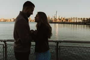 A couple embracing against a cityscape backdrop during sunset by the waterfront.