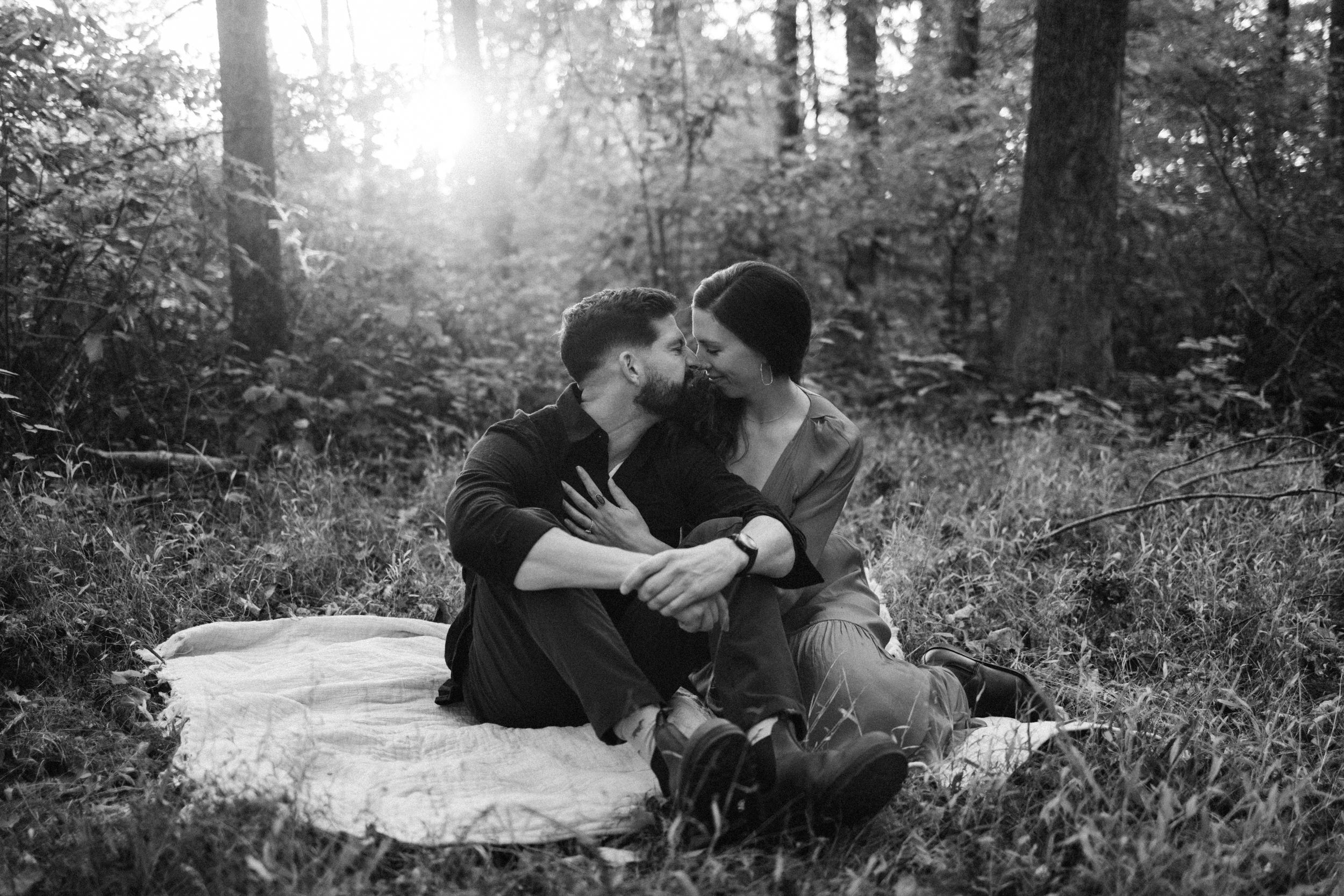Black and white portrait of couple relaxing on blanket in wooded setting.