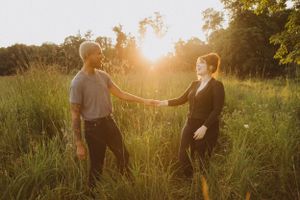 A couple connects in a golden field during sunset with arms outstretched between them.