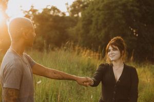Two people sharing an intimate moment while holding hands in a sun-drenched field at dusk.