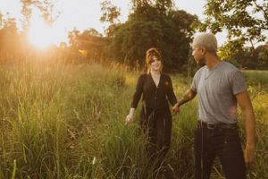 A couple walks hand in hand through a sunlit meadow during golden hour.