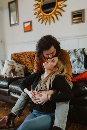 An intimate moment shared on a leather couch beneath a decorative sun mirror.
