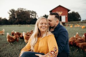 Happy couple sharing intimate moment on farm with chickens roaming in background.