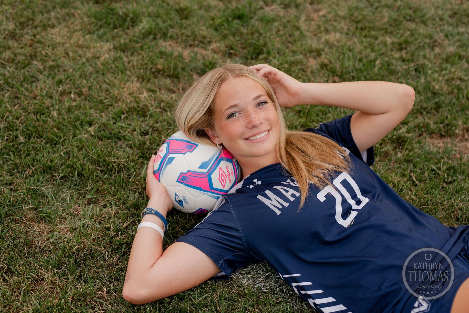 Soccer player in navy uniform poses with colorful ball on grassy field.