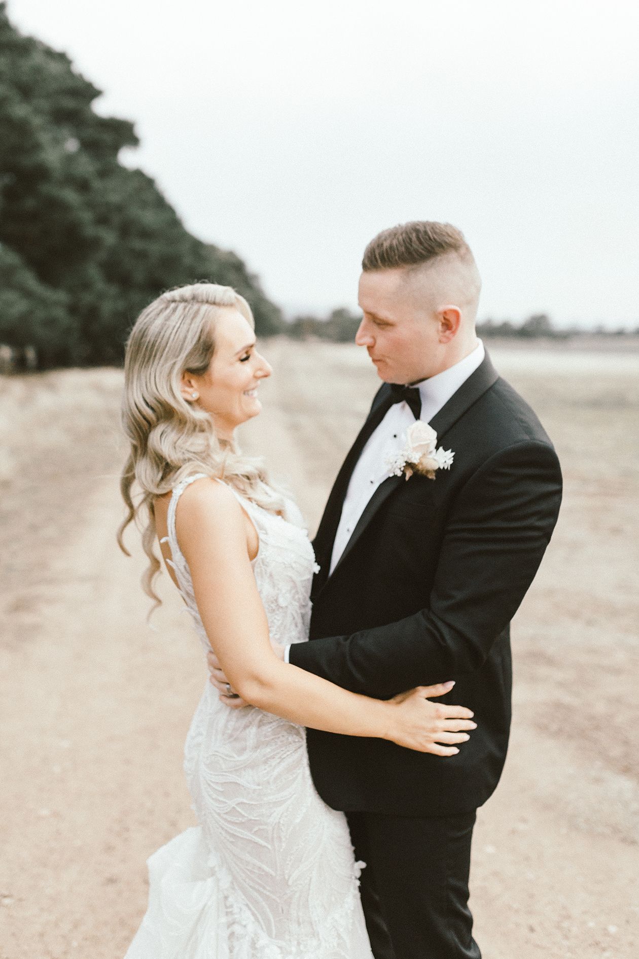 A tender moment between newlyweds on a rustic dirt path with trees in background.