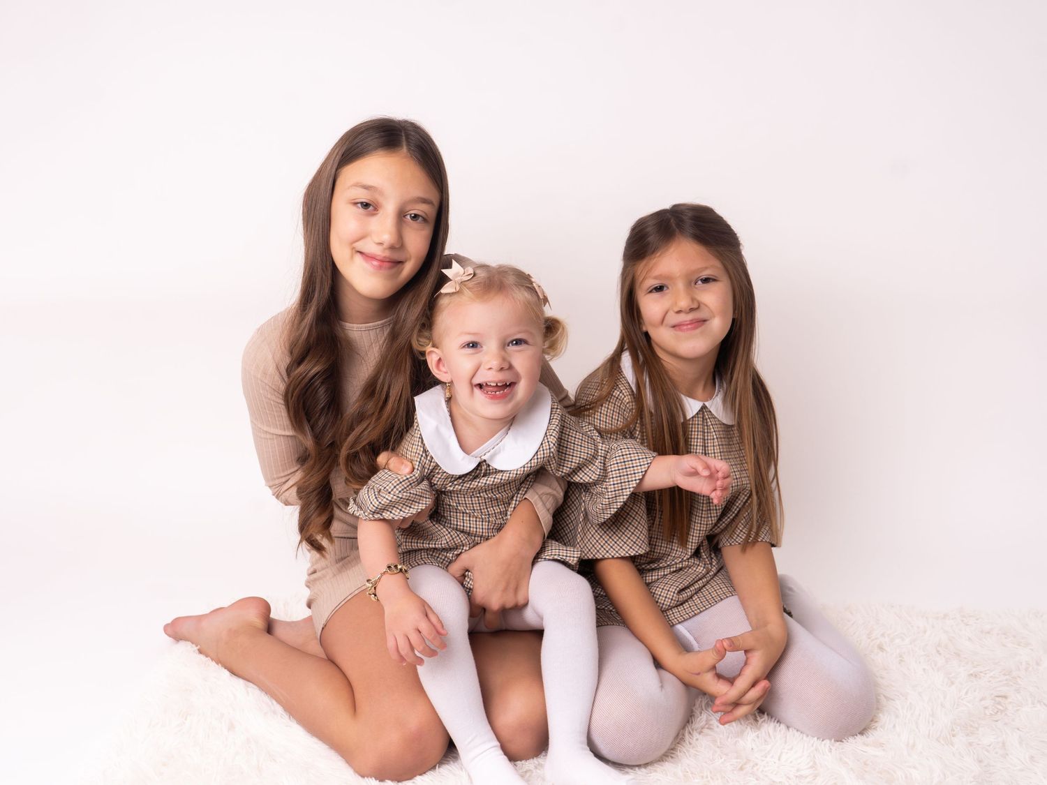 three sisters smiling during family session on white backdrop by professional newborn photographer in Doncaster.