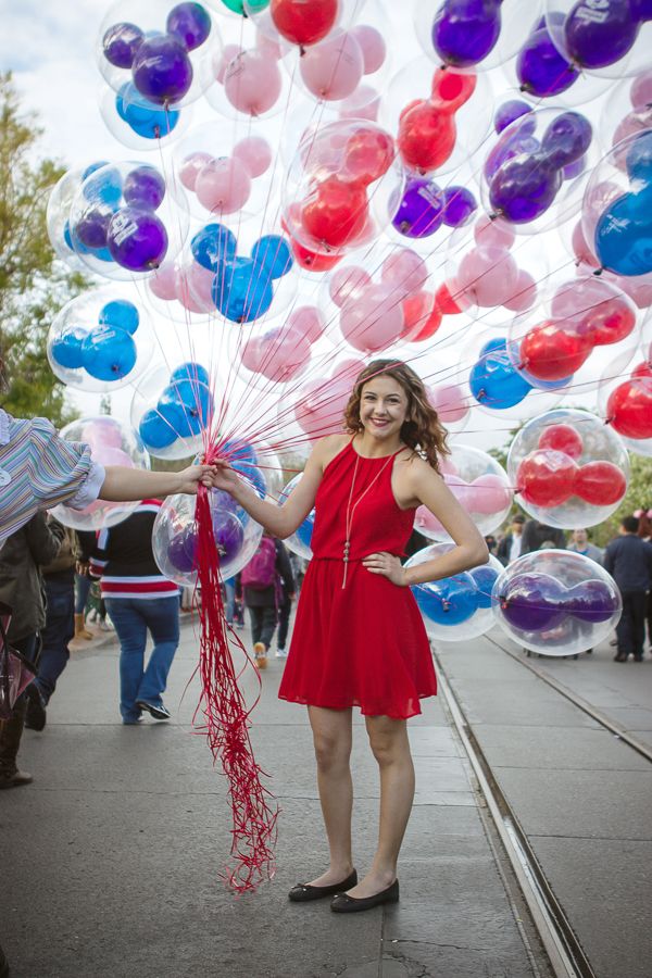 A festive scene with colorful balloons and someone in a red dress celebrating outdoors.
