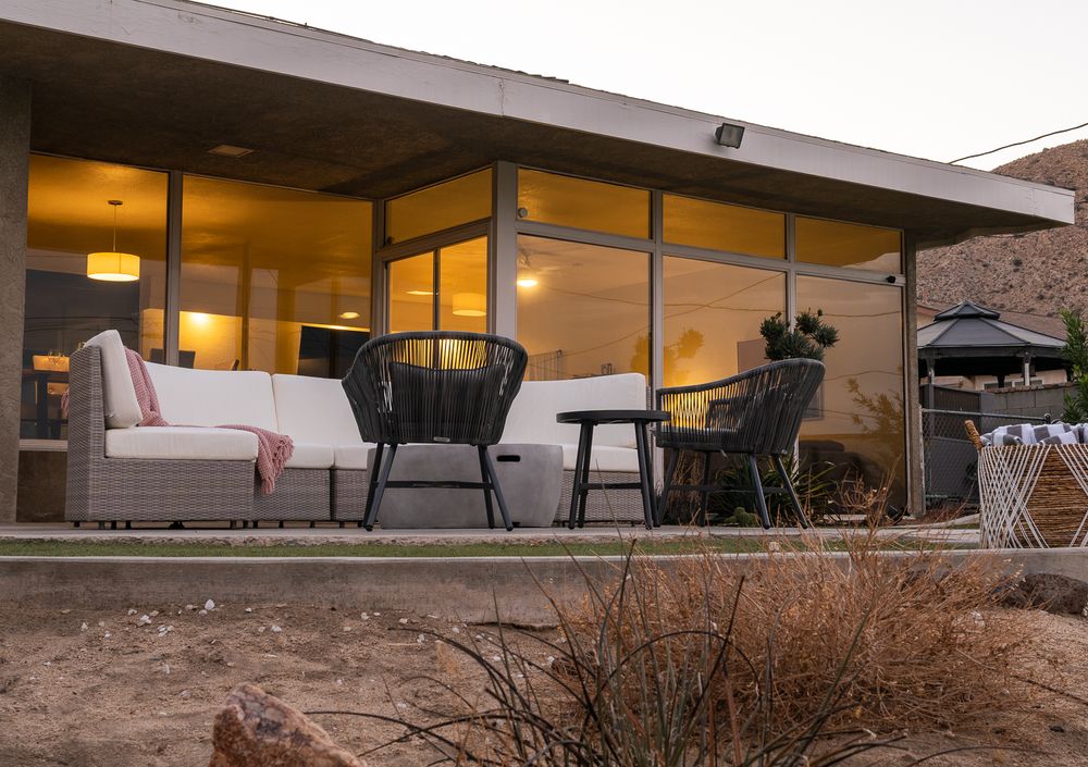 Modern desert house exterior with large windows and outdoor seating area at dusk.
