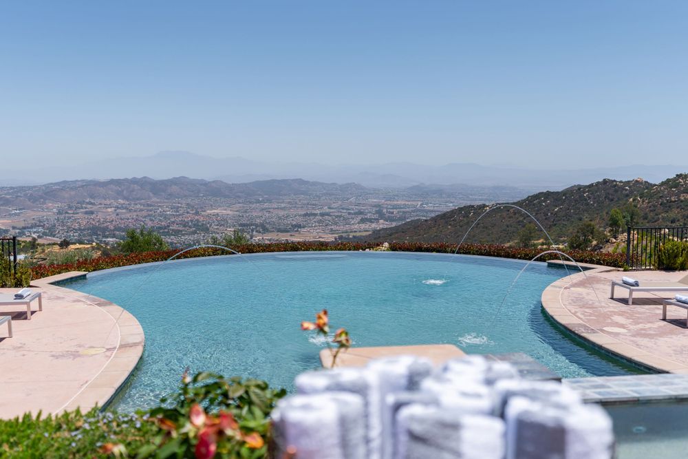 Turquoise infinity pool overlooking vast mountain landscape with loungers and umbrellas.