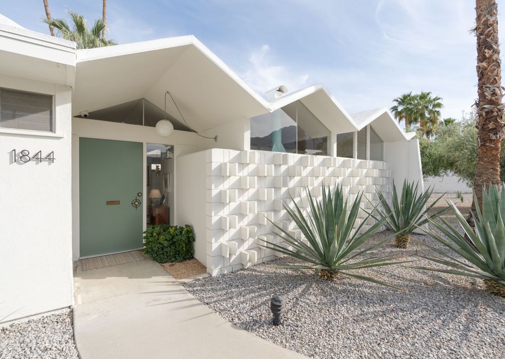 Mid-century modern home exterior with angular roof lines and desert landscaping in white and turquoise.