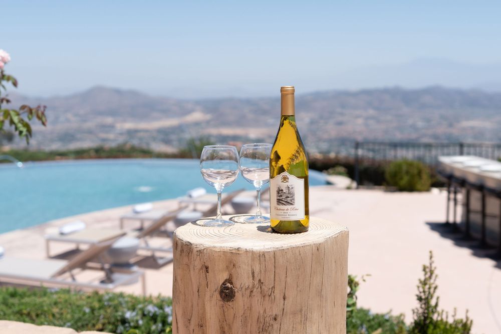 Wine bottle and glass sit on wooden table overlooking scenic beach landscape at sunset.
