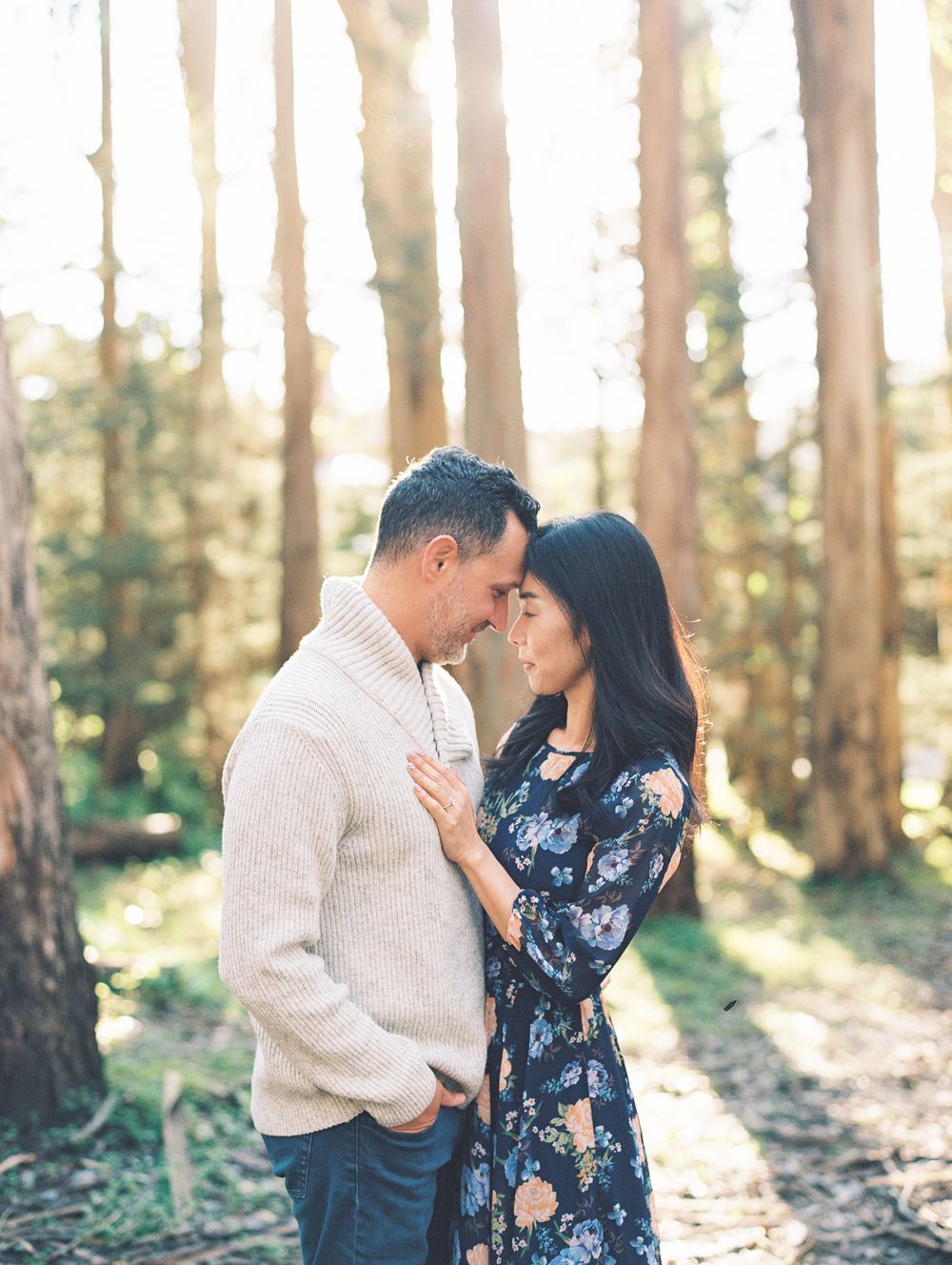 Romantic couple embracing in wooded setting with sunlight filtering through trees.