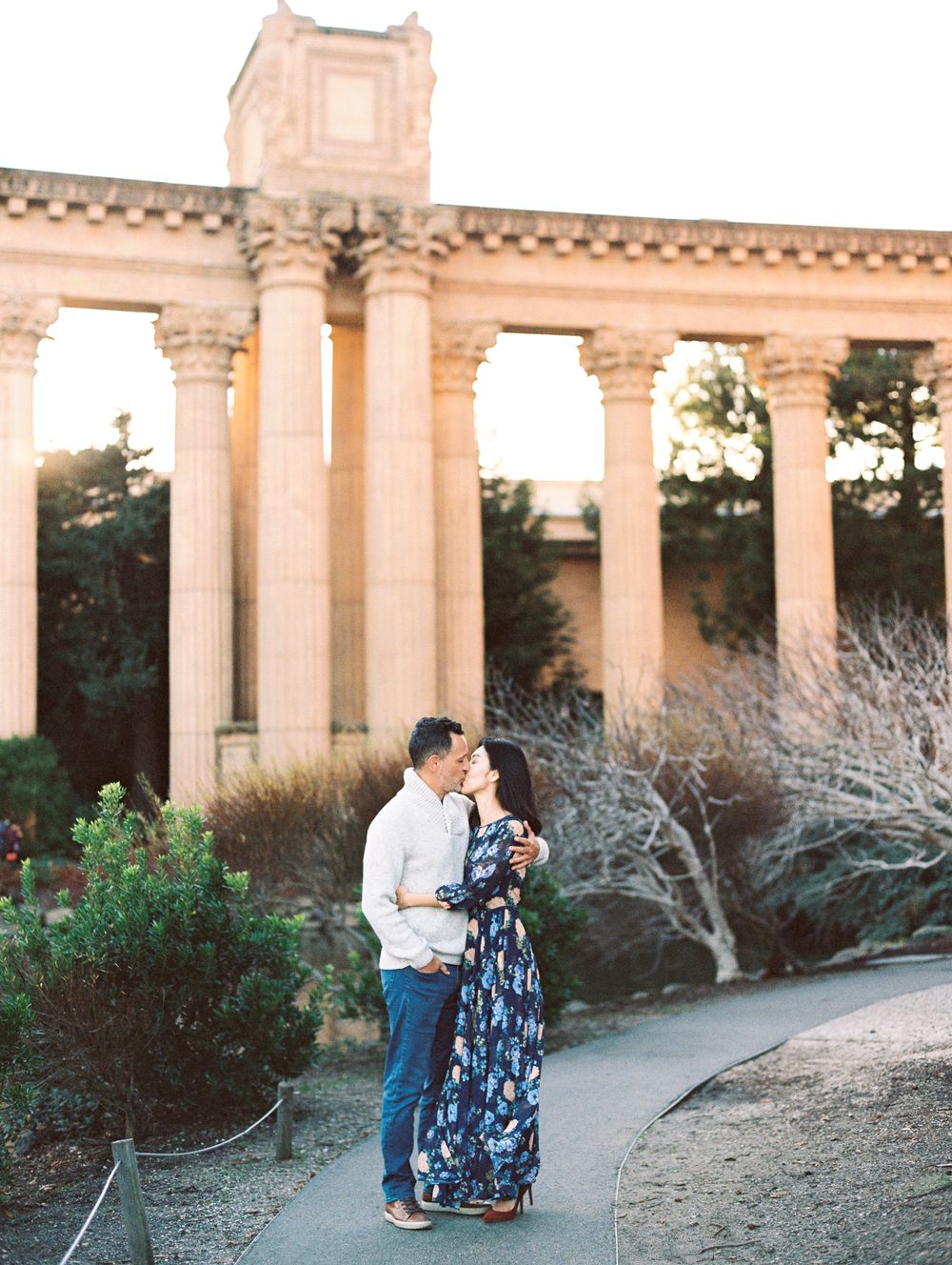 Couple sharing intimate moment beneath classical architecture columns at sunset.