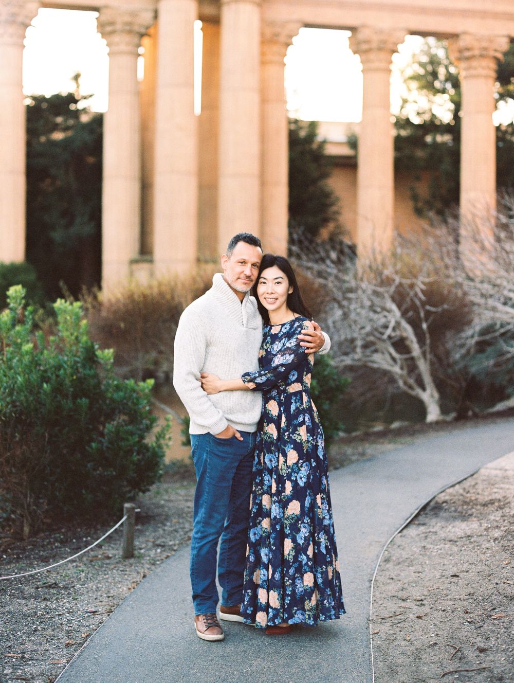Happy couple embraces on path near classical columns and garden.