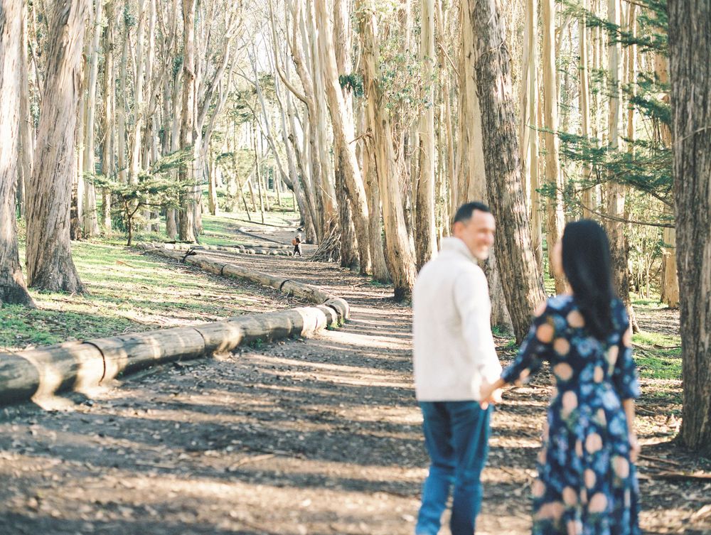 Two people in casual attire stroll together on a wooded trail surrounded by eucalyptus trees.