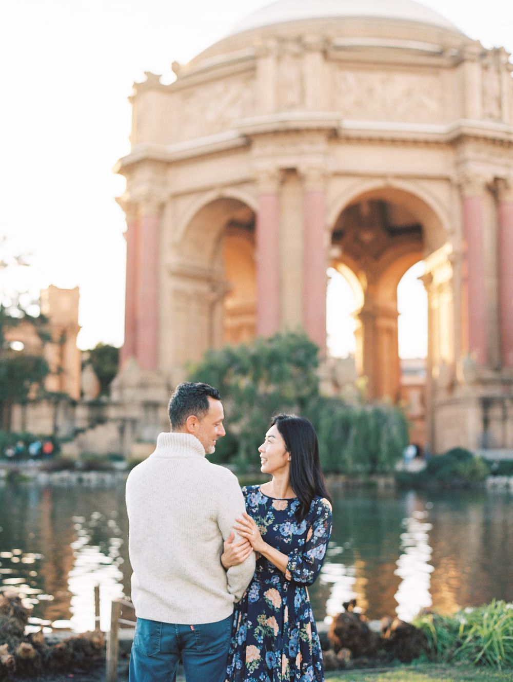 Romantic couple shares tender moment by Palace of Fine Arts reflecting pool at golden hour.
