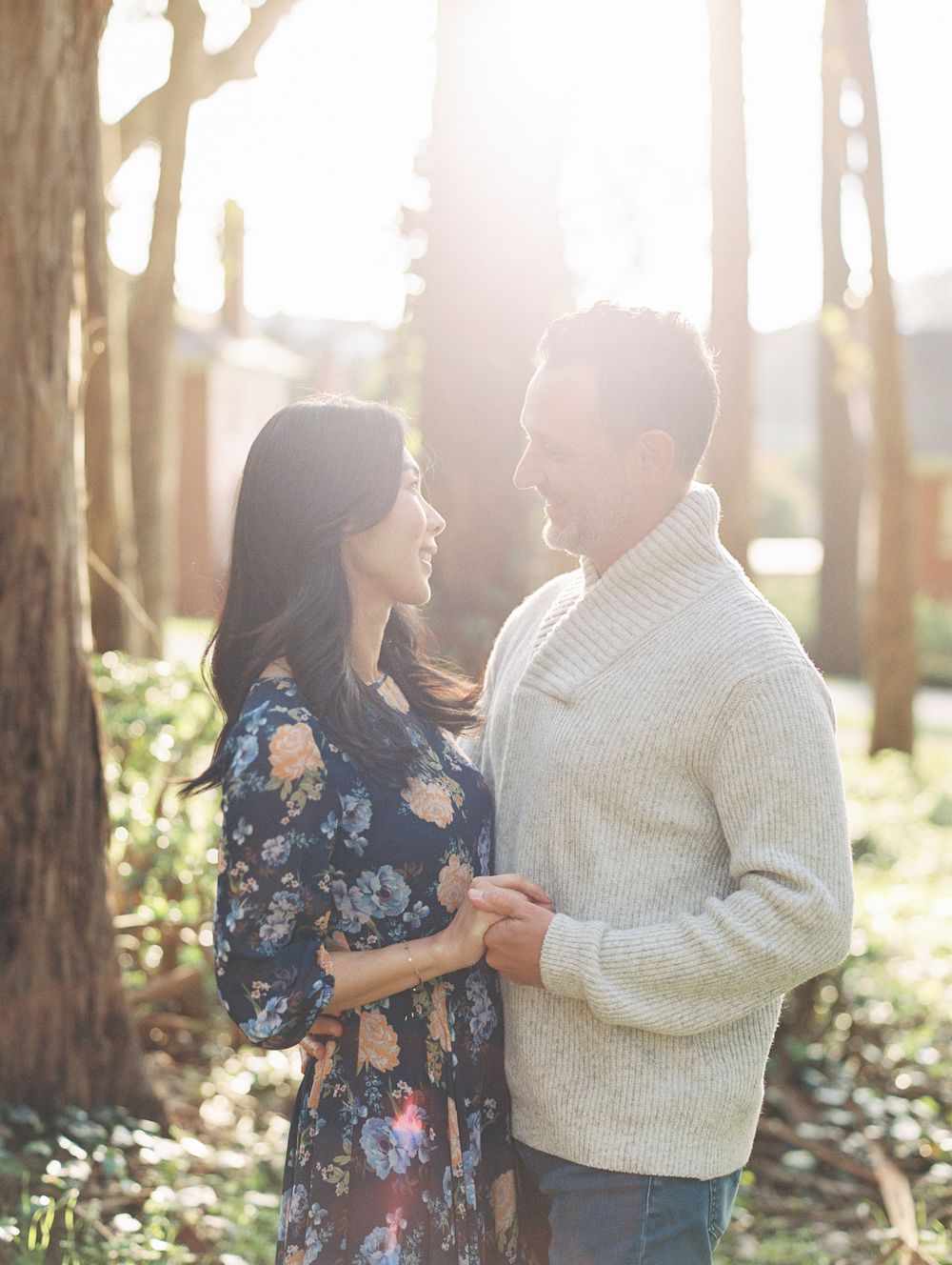 A romantic forest photoshoot featuring a couple in a white sweater and floral dress holding hands.