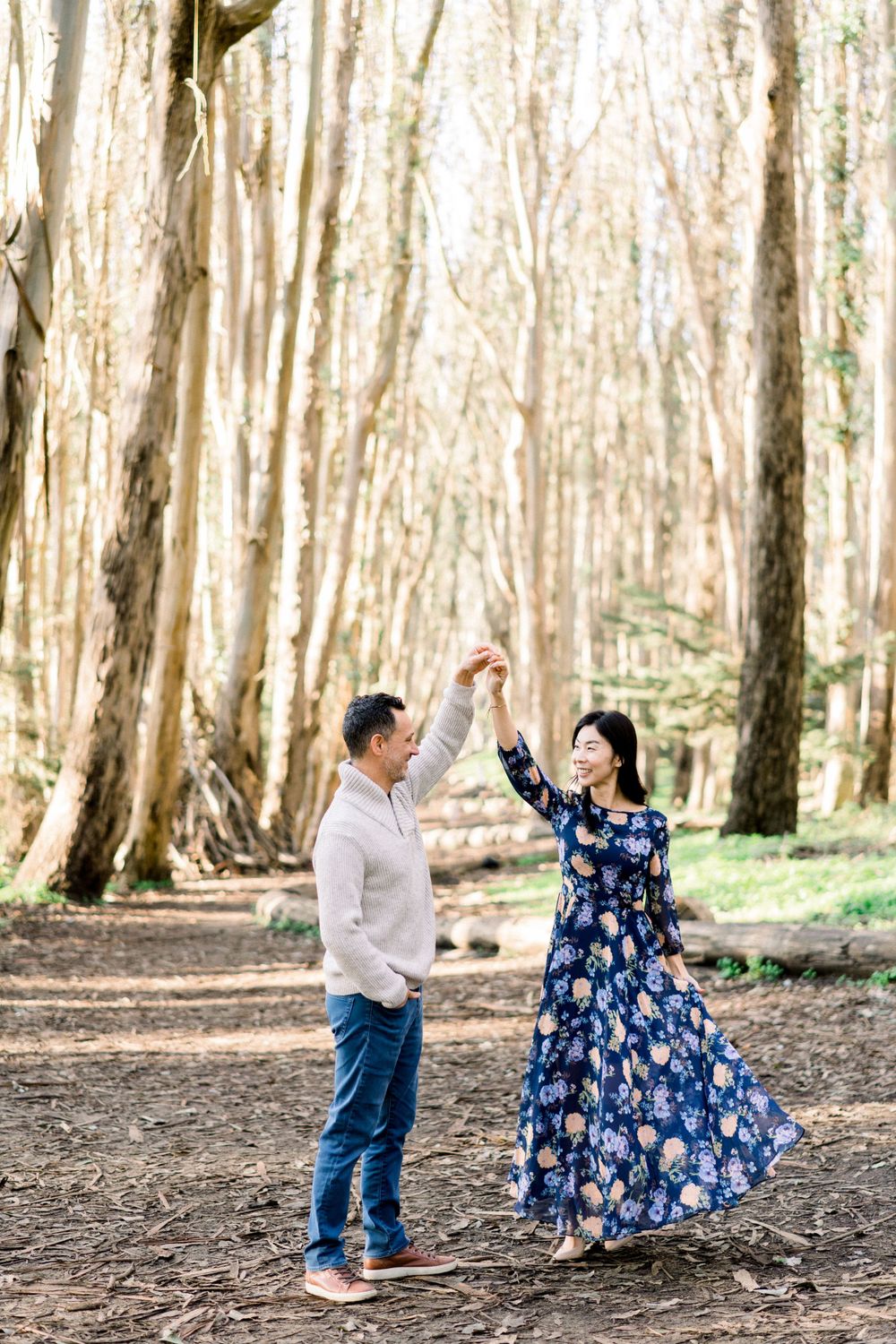 A joyful dancing moment between a couple on a forest path wearing complementary outfits.