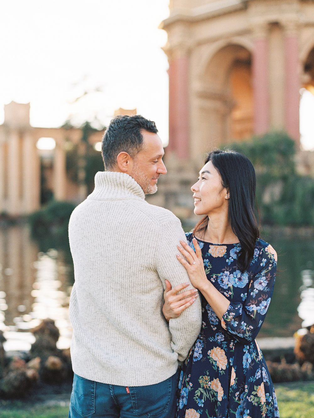 A couple embracing by the Palace of Fine Arts reflection pool at golden hour.