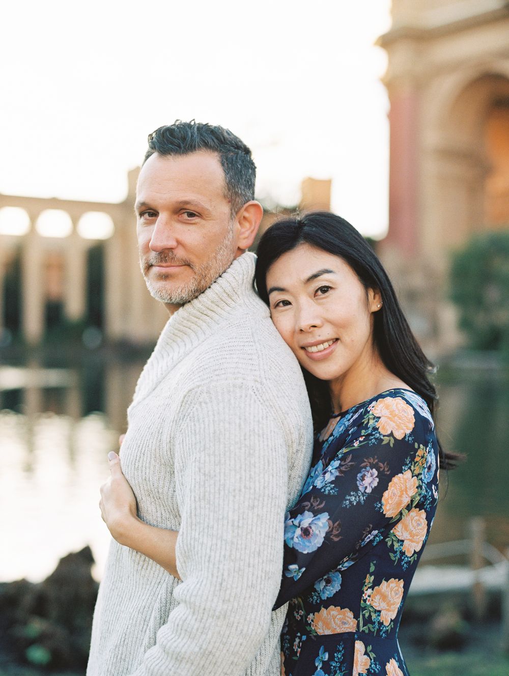 Couple in coordinated outfits pose against architectural backdrop with reflecting pool.
