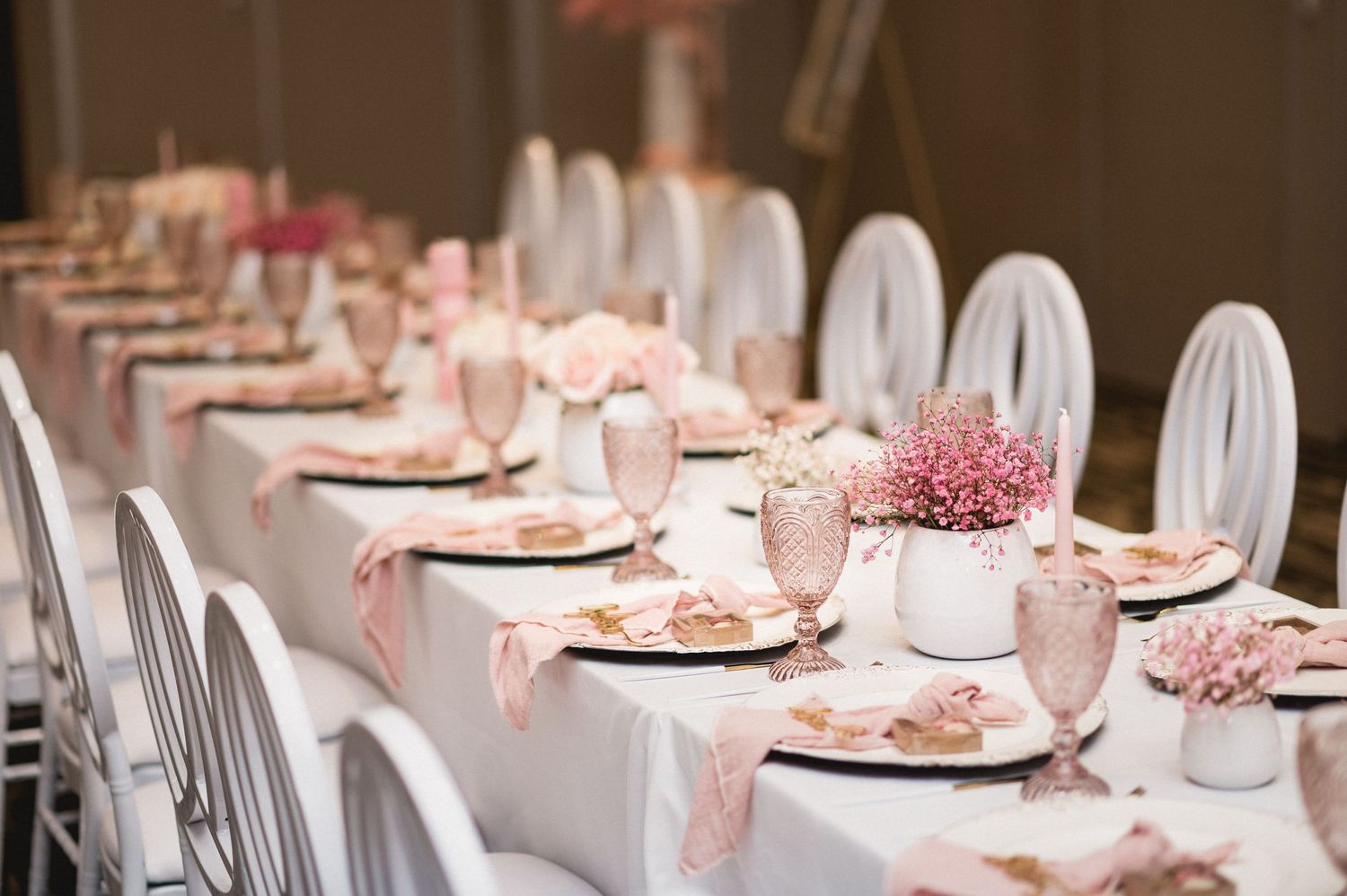 Elegant table setting with pink and white decor featuring place settings and floral centerpieces at a formal event.