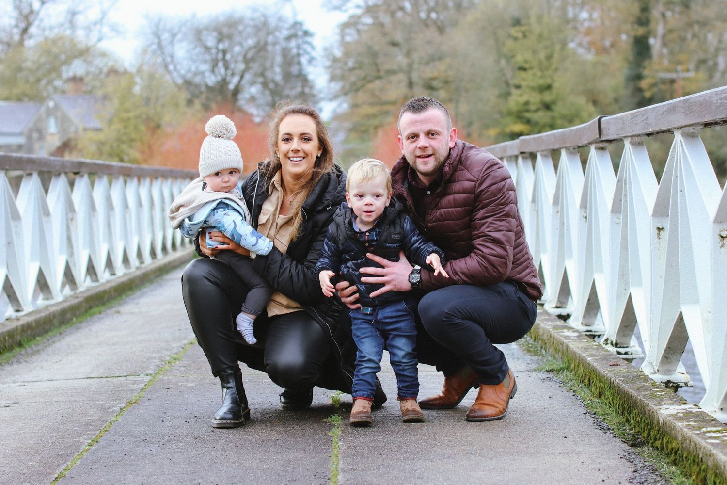 Family kneeling together on a white bridge walkway during autumn.