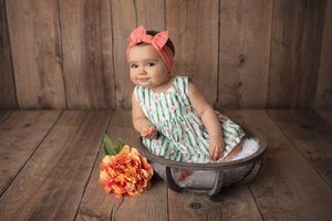 Child in striped dress sits in vintage metal tub with orange flower decoration.