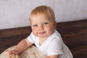 Child in white shirt smiles while leaning on rustic wooden surface.