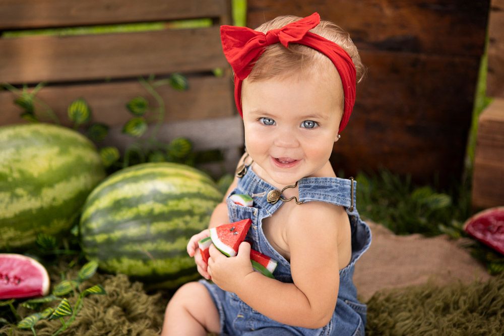 Summer portrait with red bow and denim outfit among fresh watermelons.
