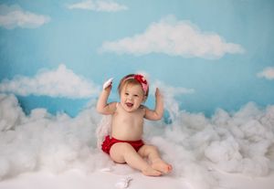 Cloud-themed photo setup with red bow and matching bottoms against blue sky backdrop.