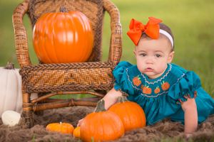 Fall themed photo with pumpkins and baby in teal dress with orange bow.