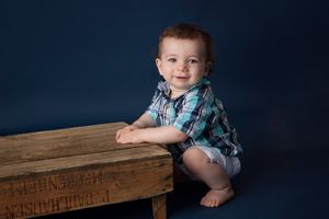 Child in plaid shirt poses next to wooden table against dark blue background.