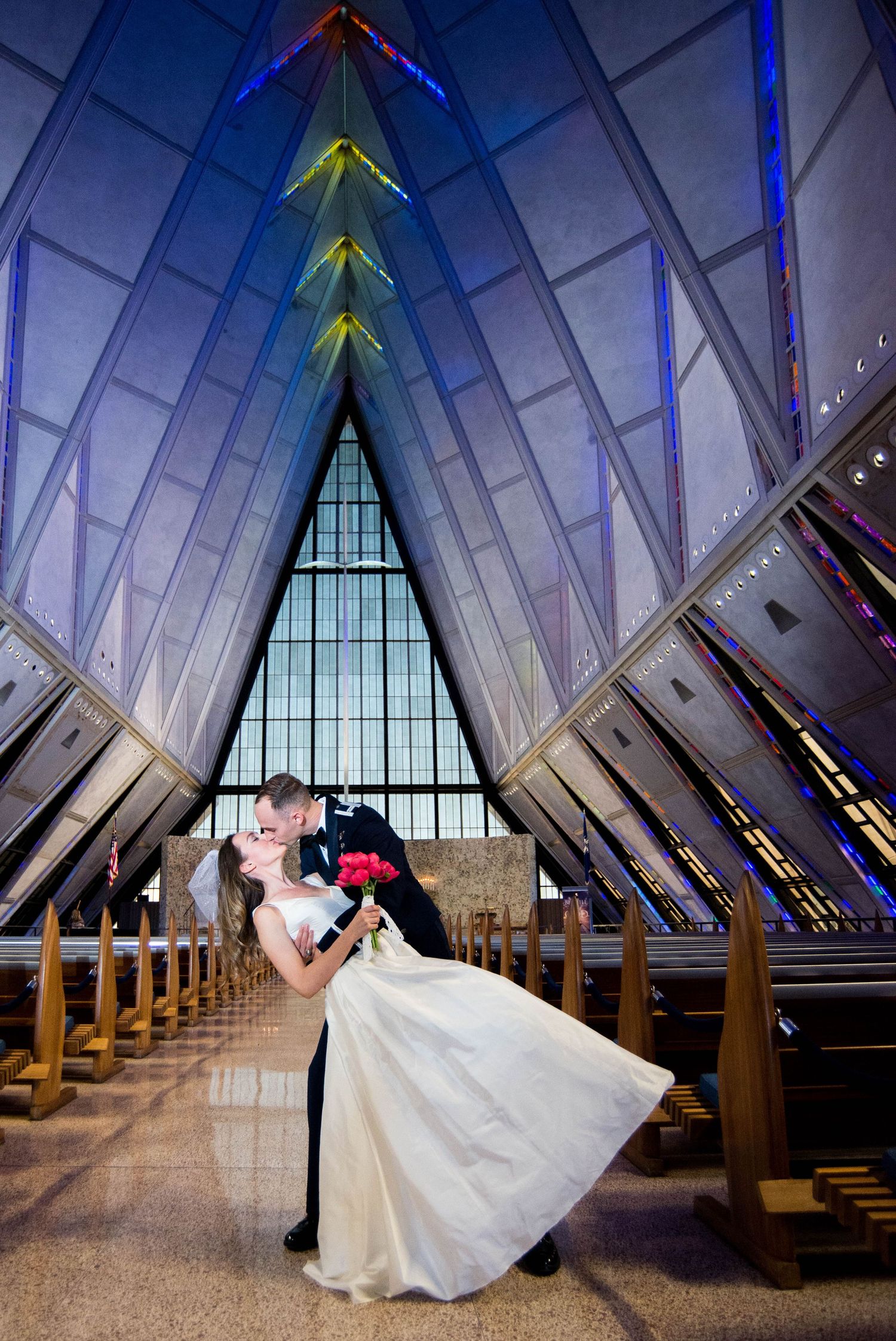 A romantic wedding couple shares an intimate moment in a stunning modern chapel with dramatic angular architecture and lighting.