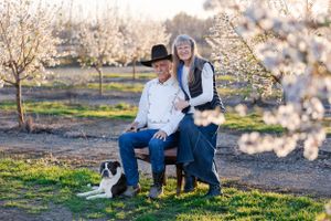 couple in blooming almond with chair and dog orchard orland, california