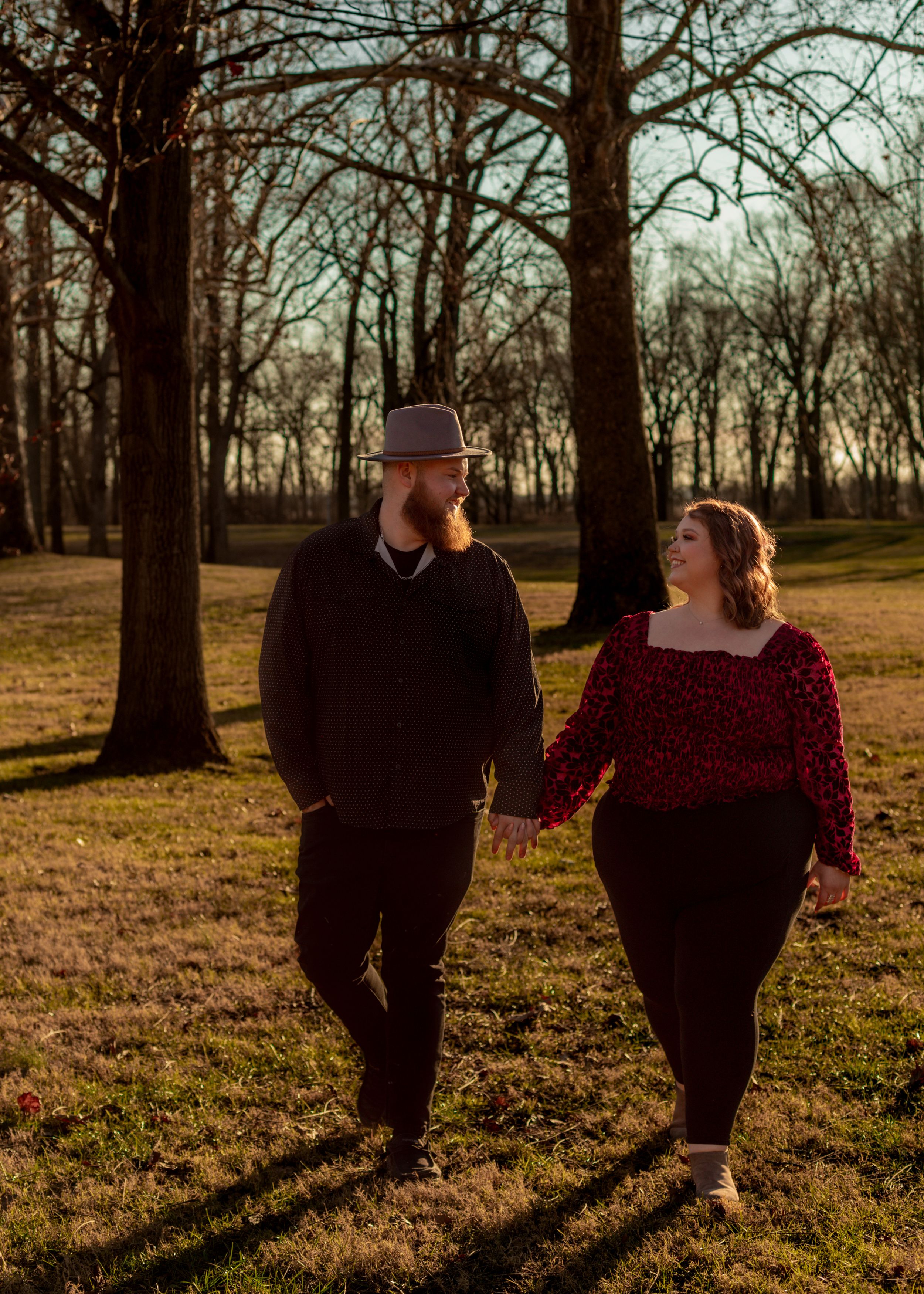 Couple walking together through park at sunset casting long shadows.