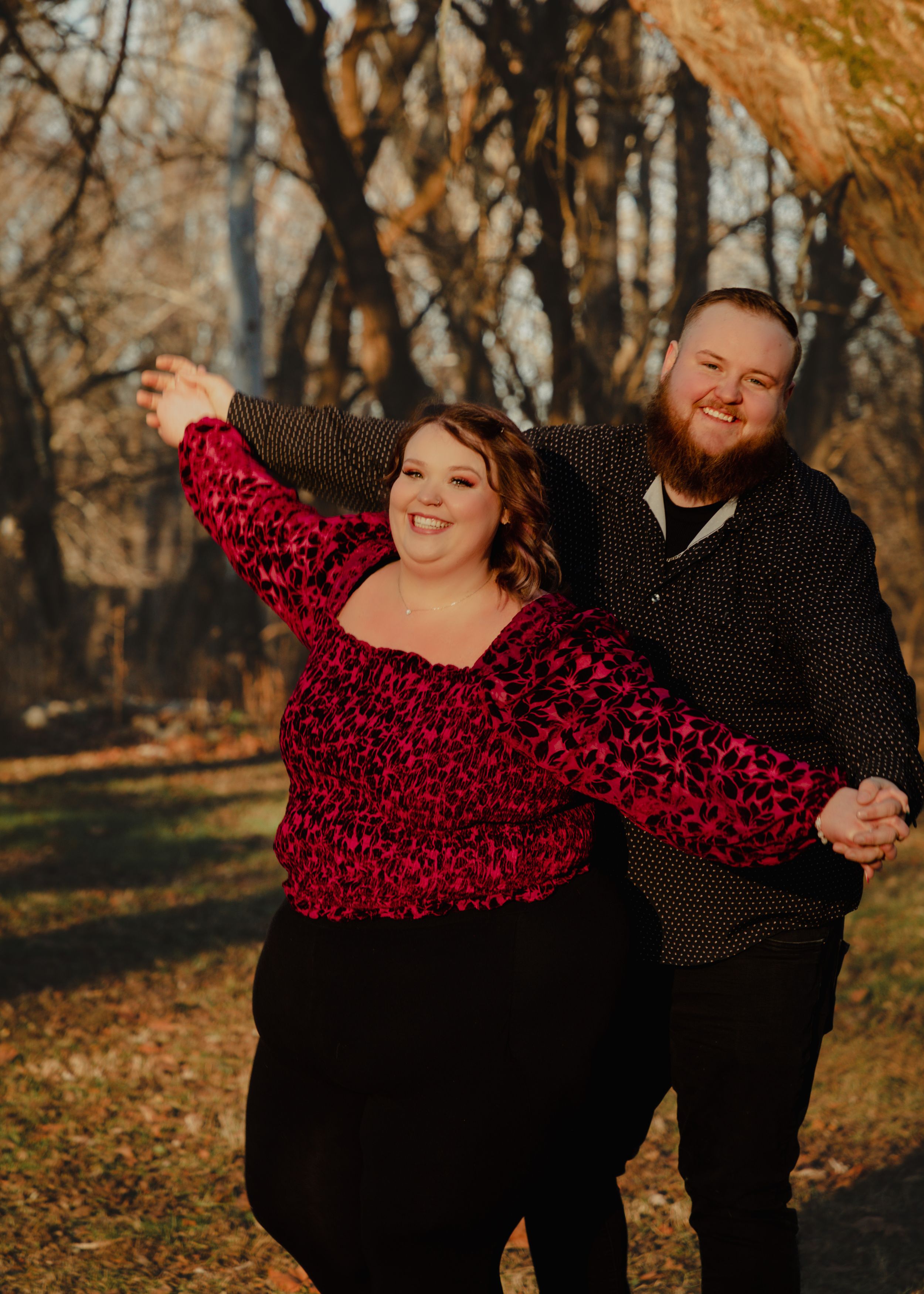 Couple in black and red outfits share joyful moment in fall woodland setting.