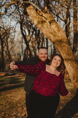 Couple in coordinated outfits pose playfully against autumn trees at sunset.