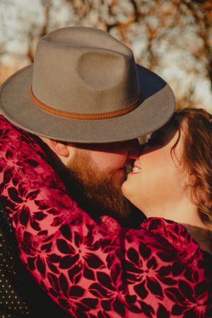 Close-up of couple with brown fedora hat sharing intimate moment against autumn background.