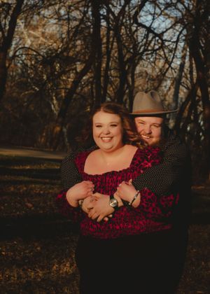 Playful couple in black and red clothing laughing together in wooded park.