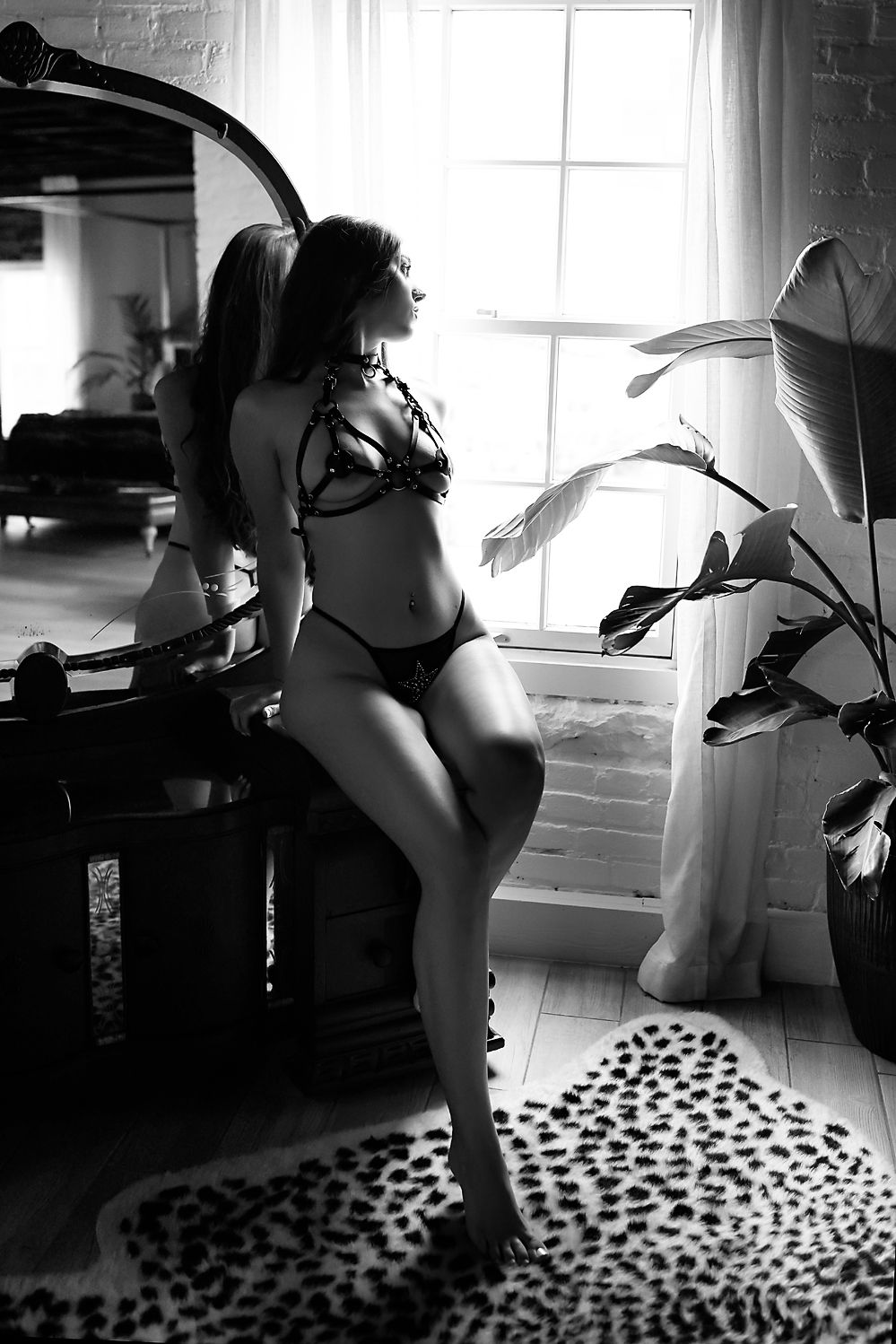 Black and white portrait near window with leopard rug and dramatic lighting effects.