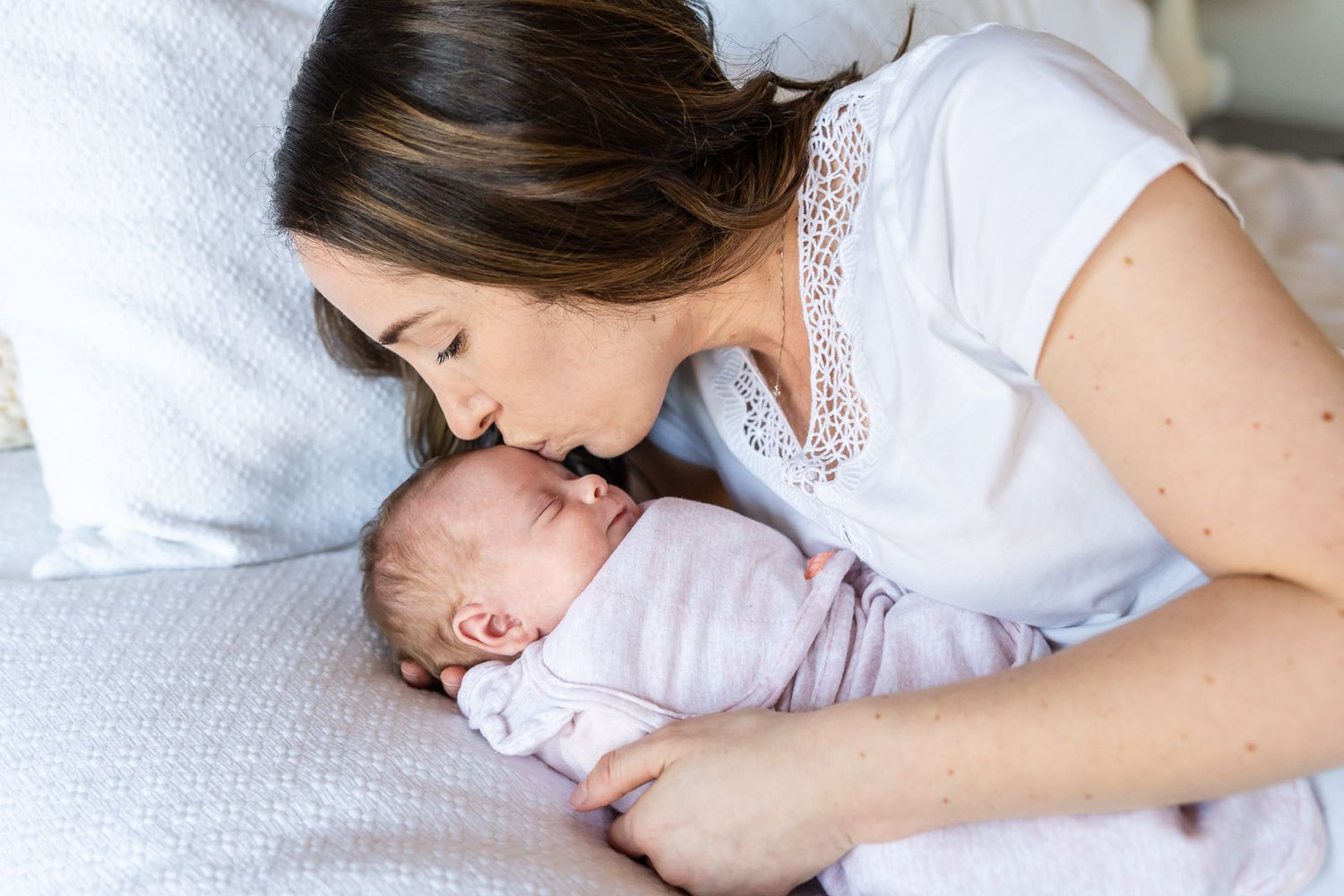 Mom kissing baby girl on their bed.