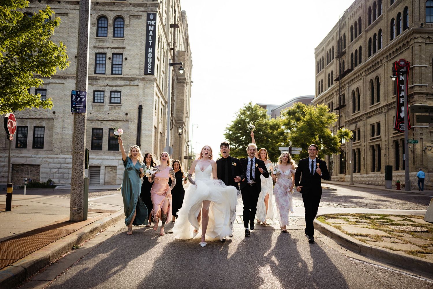 Wedding party walks down urban street with historic buildings in background.