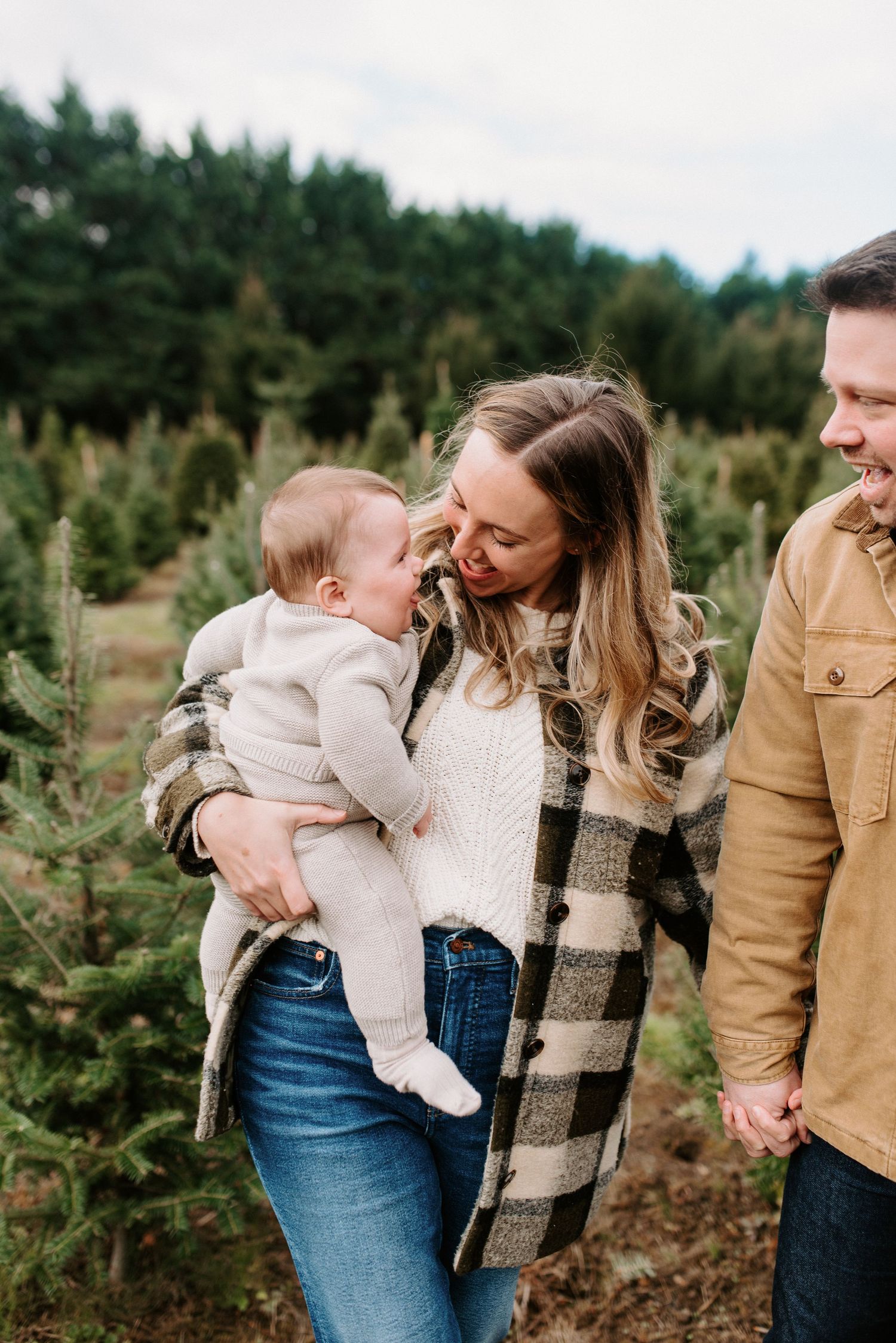 Family sharing playful moments among Christmas trees at a tree farm.